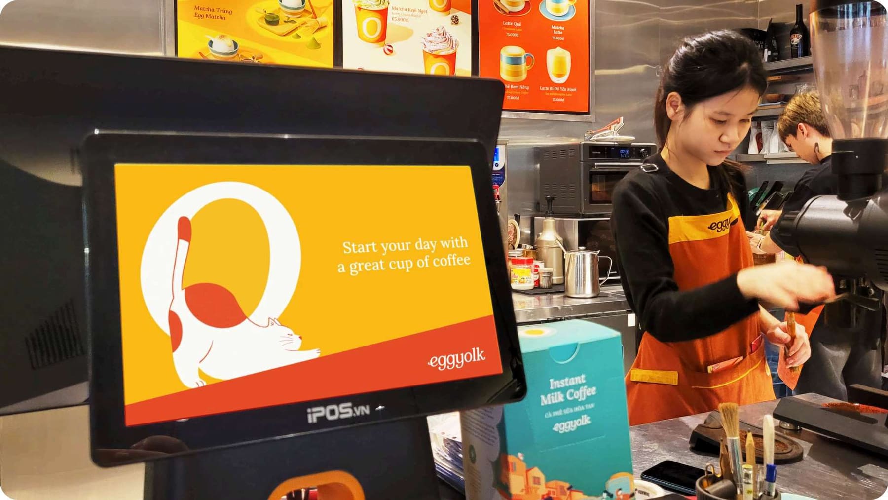 An Eggyolk barista at work behind the counter, with a sunny welcome screen at the till
