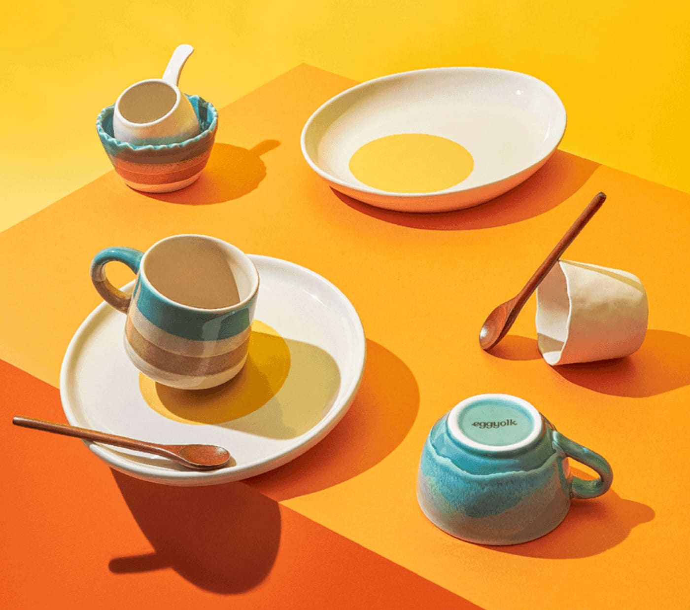Eggyolk ceramic egg cups, plates and spoons on a bright orange table